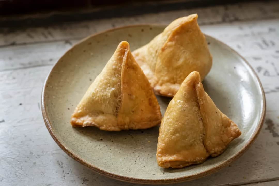 Crispy golden-brown samosas filled with spiced potato and peas, garnished with cilantro.