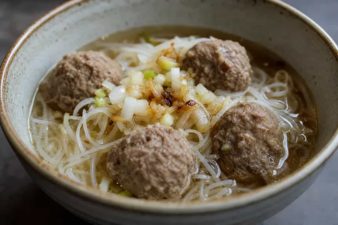Bowl of Indonesian beef bakso soup with meatballs, noodles, and herbs garnished on top.