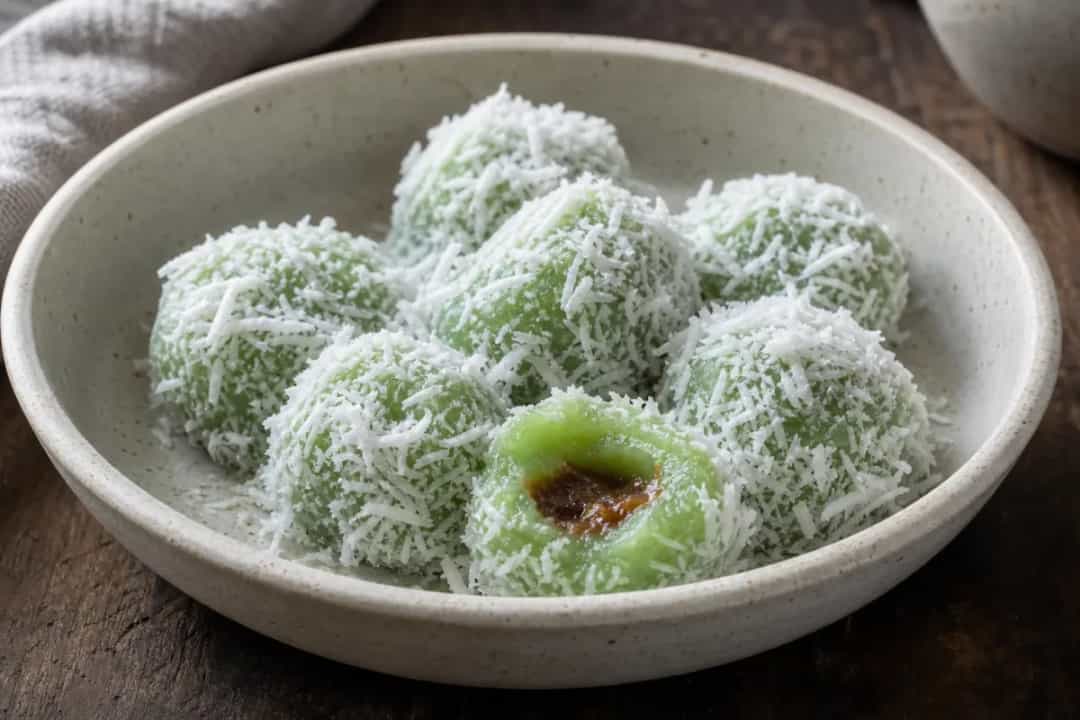 Chewy green rice cakes coated in grated coconut, showcasing palm sugar filling.