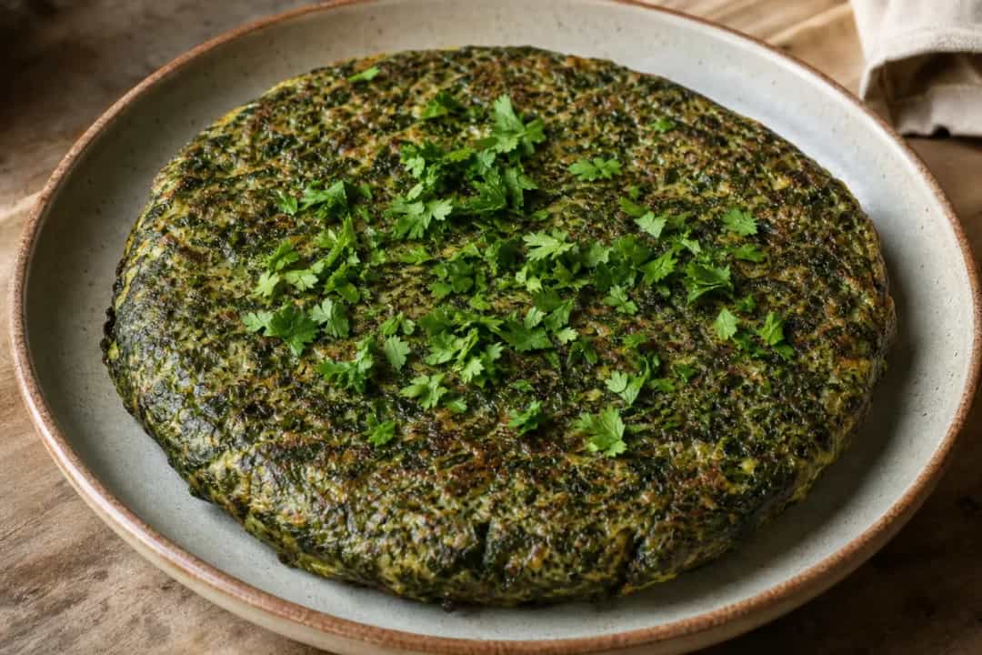 Plated Iranian Kuku Sabzi showing vibrant green herbs, golden edges, and a fluffy texture.