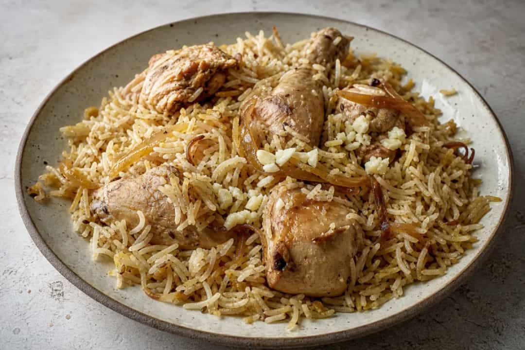 A vibrant plate of Iraqi biryani featuring tender chicken, colorful spices, and fluffy rice garnished with herbs.
