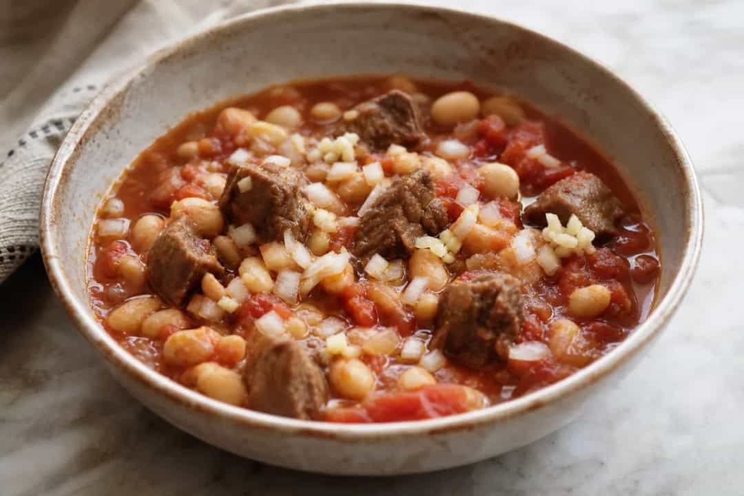 A comforting bowl of Iraqi Fasolia with tender beef, white beans, and vibrant tomato sauce garnished with fresh herbs.