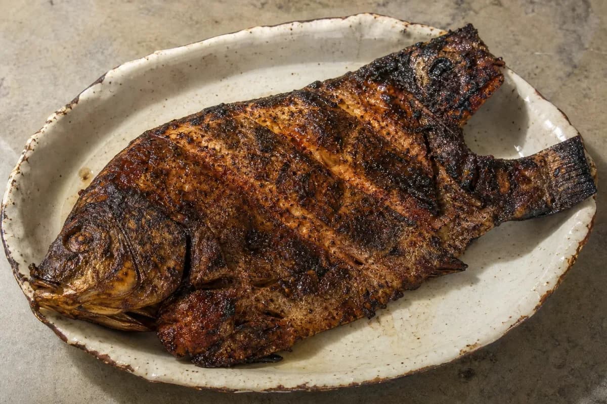 Grilled fish served with tamarind sauce, garnished with spices and herbs.