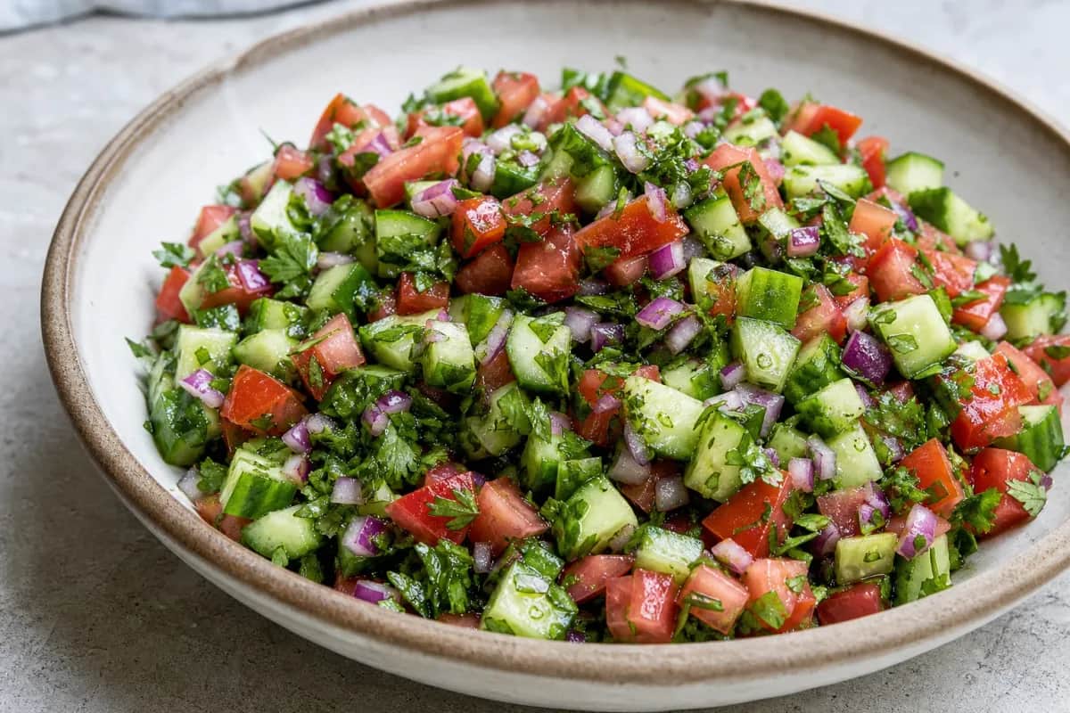 Colorful chopped salad with diced cucumbers, tomatoes, and herbs in a bowl.
