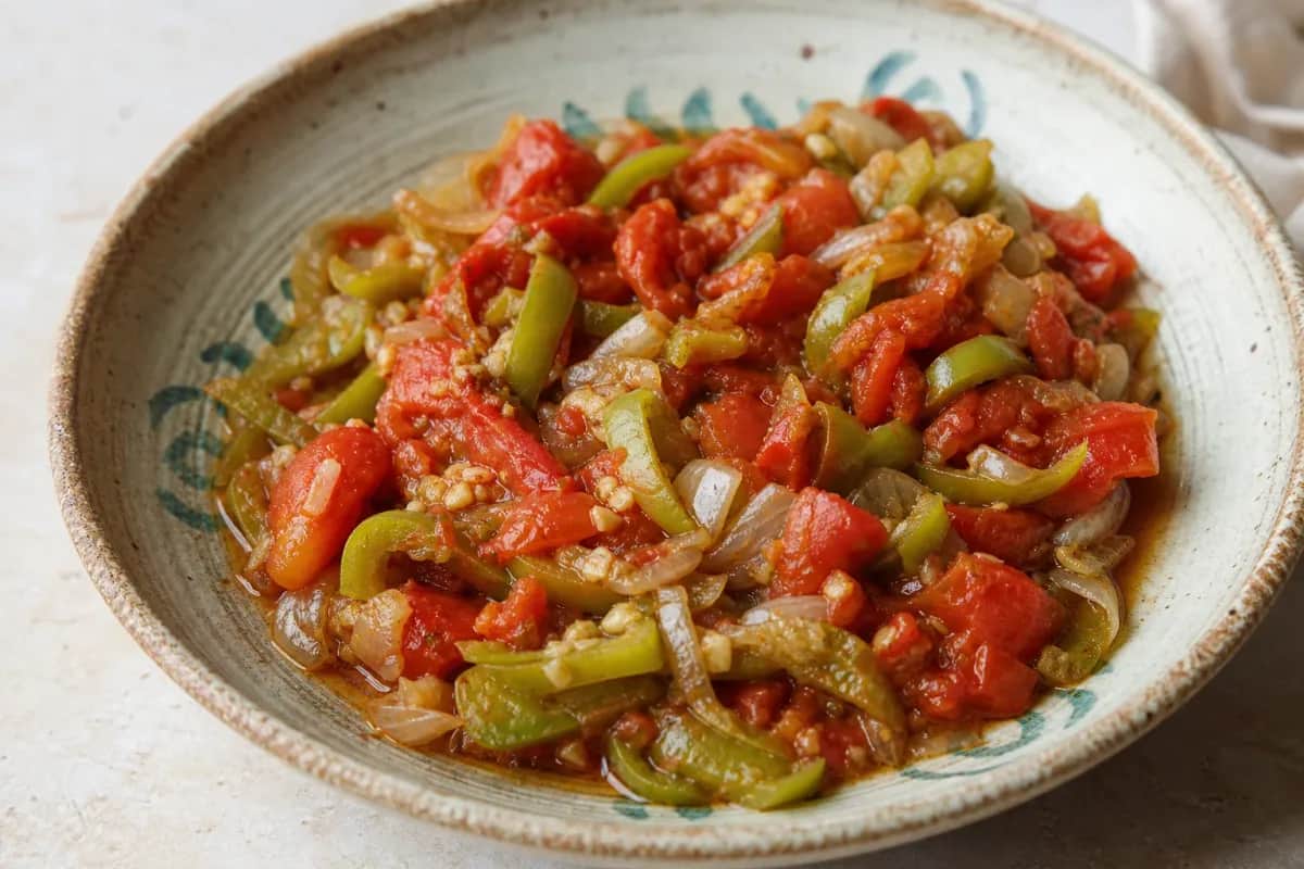 A vibrant plate of Galayet Bandora featuring sautéed tomatoes, green peppers, and a drizzle of olive oil, garnished with herbs.