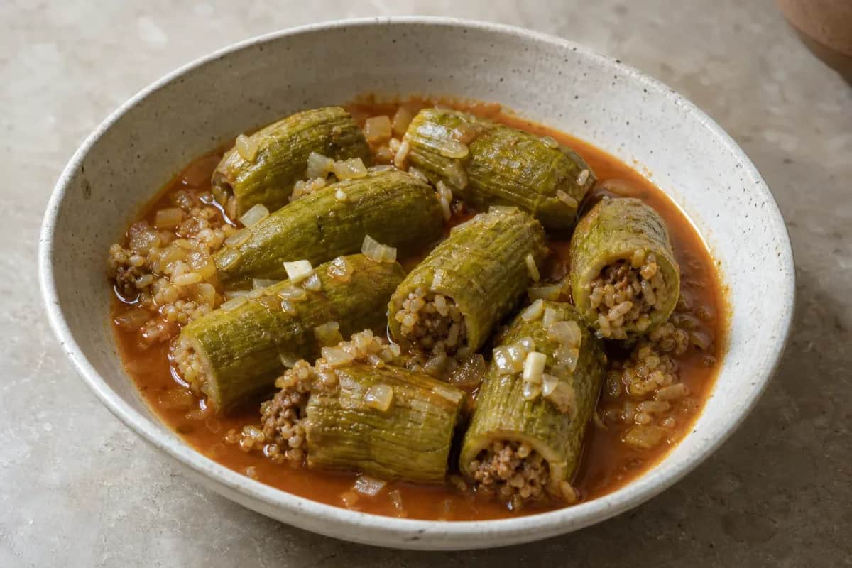 Plated Kousa Mahshi showcasing stuffed zucchini in rich tomato broth, garnished with herbs.