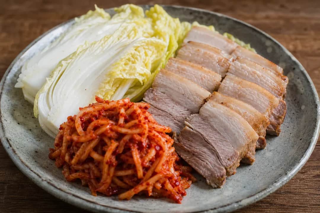 Plated Korean Bossam with succulent pork belly, fresh lettuce, and vibrant spicy radish pickles arranged neatly.