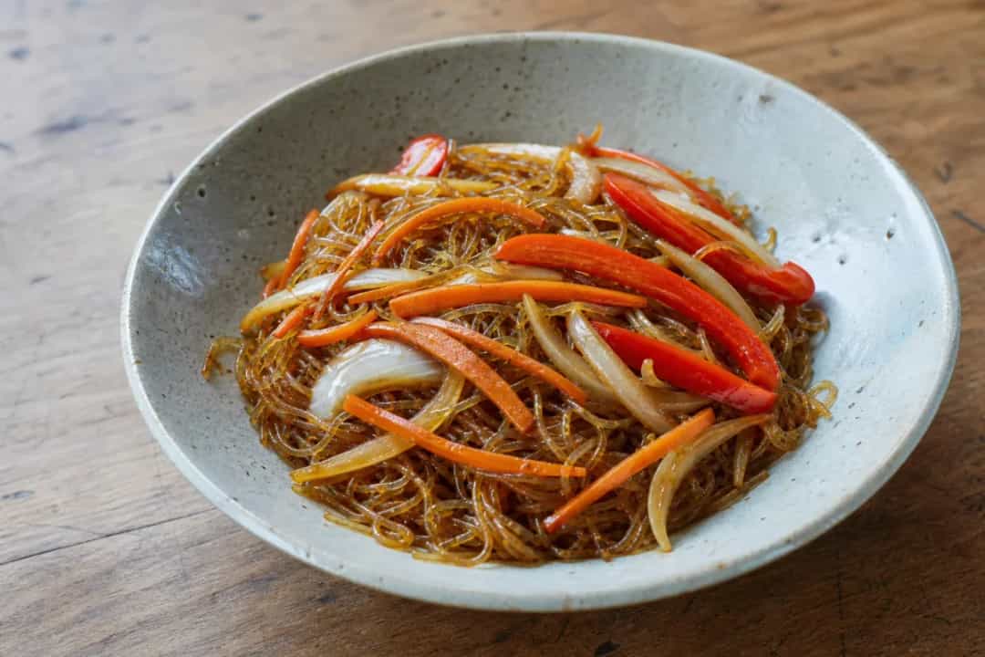 Colorful stir-fried glass noodles with vegetables garnished in a bowl.