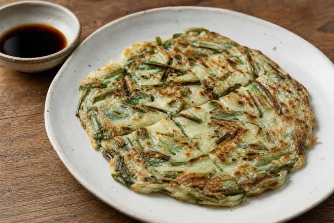 Golden-brown Korean pancakes topped with green scallions, served with a soy dipping sauce.
