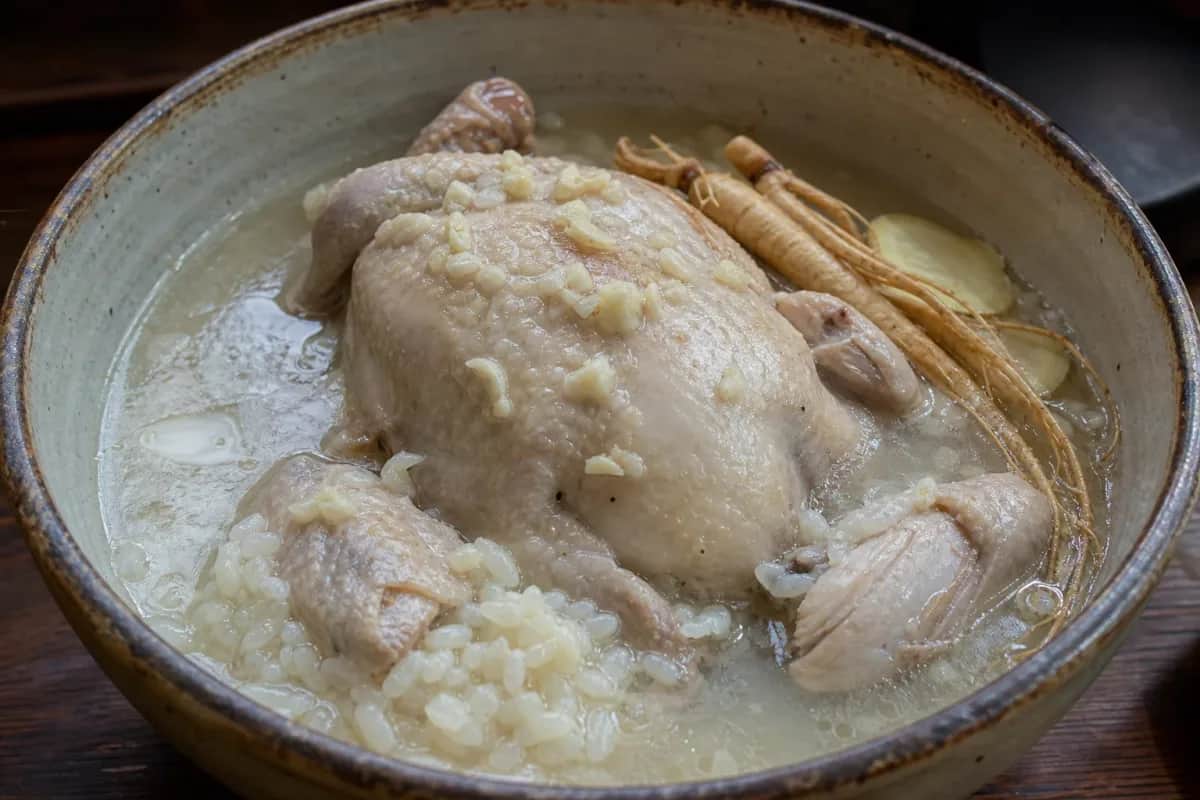 A bowl of Korean Samgyetang with tender chicken, sticky rice, and ginseng, garnished with green onions.