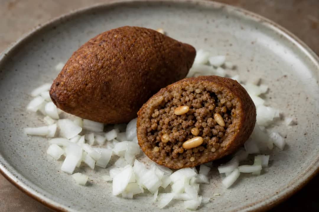 Golden-brown kubba stuffed with spiced beef, garnished with herbs and served on a plate.
