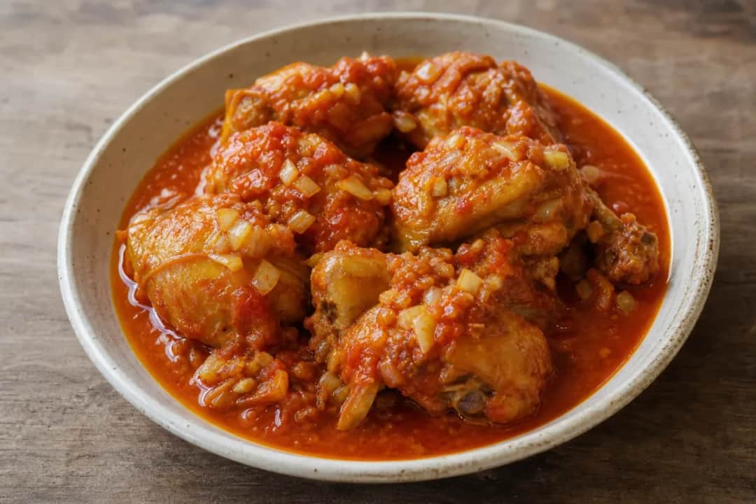 Tender chicken pieces in a rich, spicy tomato sauce garnished with herbs and served on a plate.