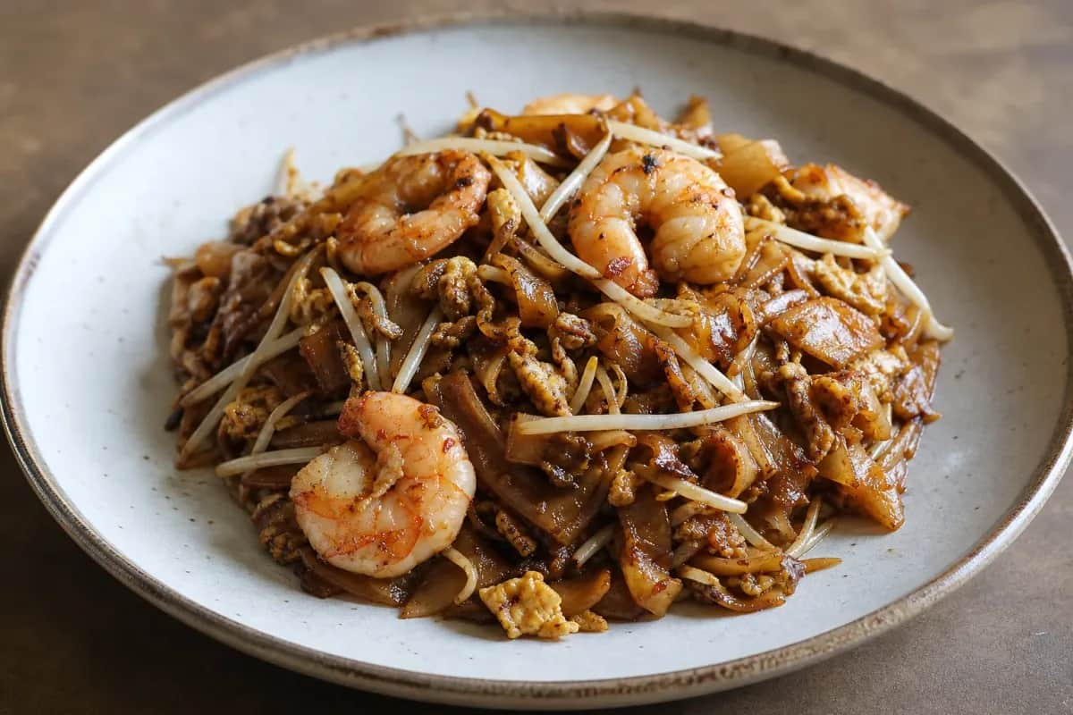 Plate of Char Kway Teow with prawns, egg, and fresh bean sprouts, showcasing a glossy texture and vibrant colors.