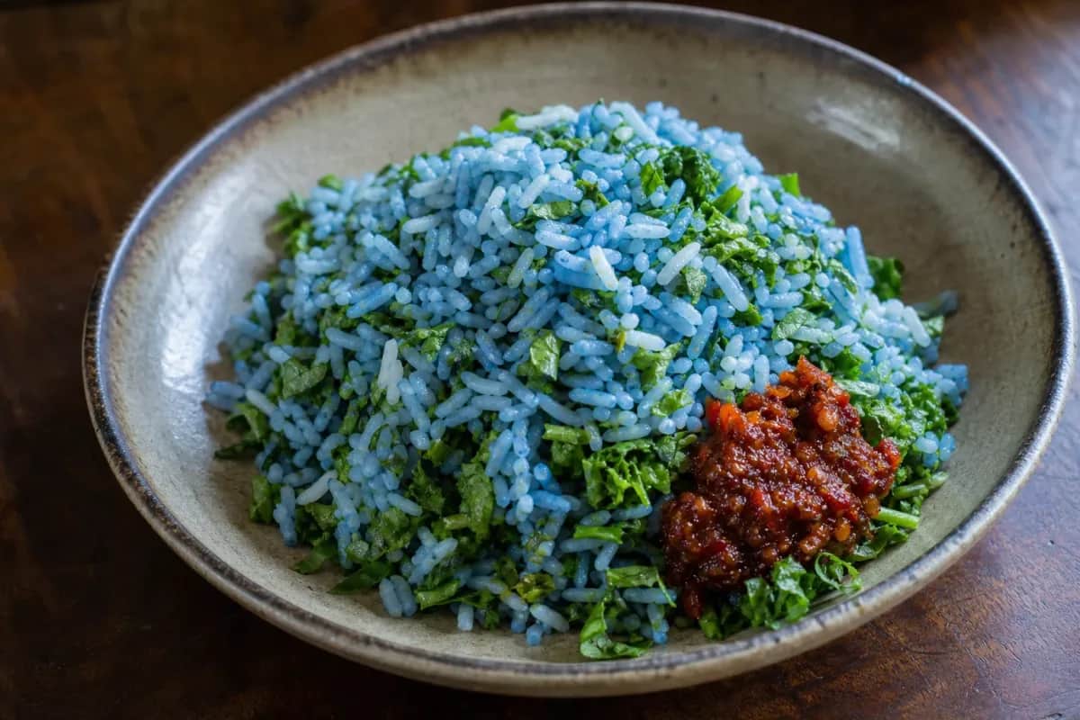 Colorful plate of Nasi Kerabu with blue rice, herbs, and sambal served attractively.