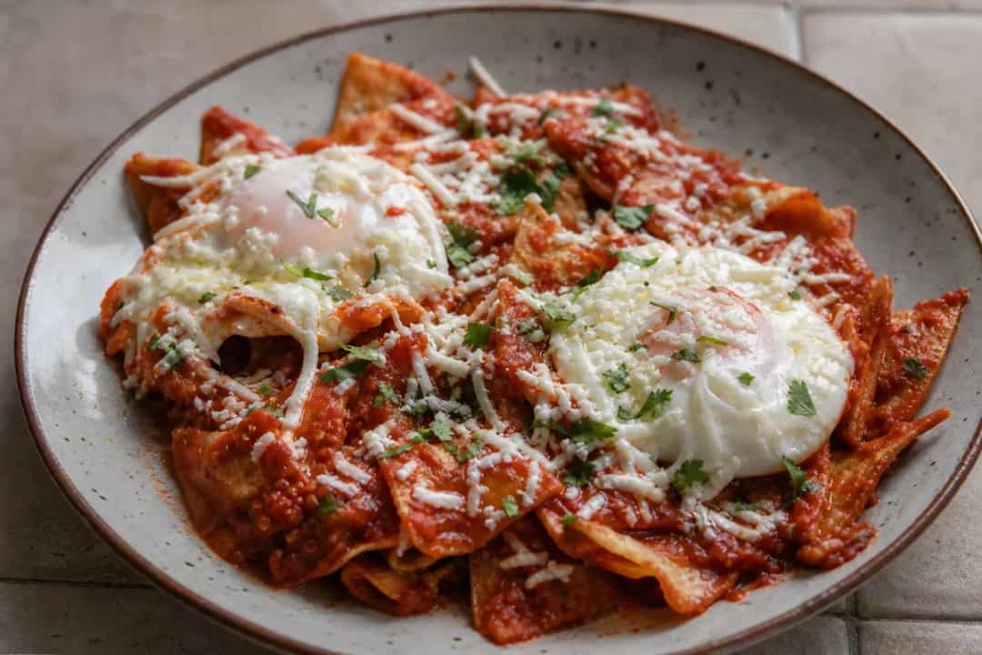 Plated chilaquiles with red sauce, topped with fried eggs and crema, garnished with cilantro.