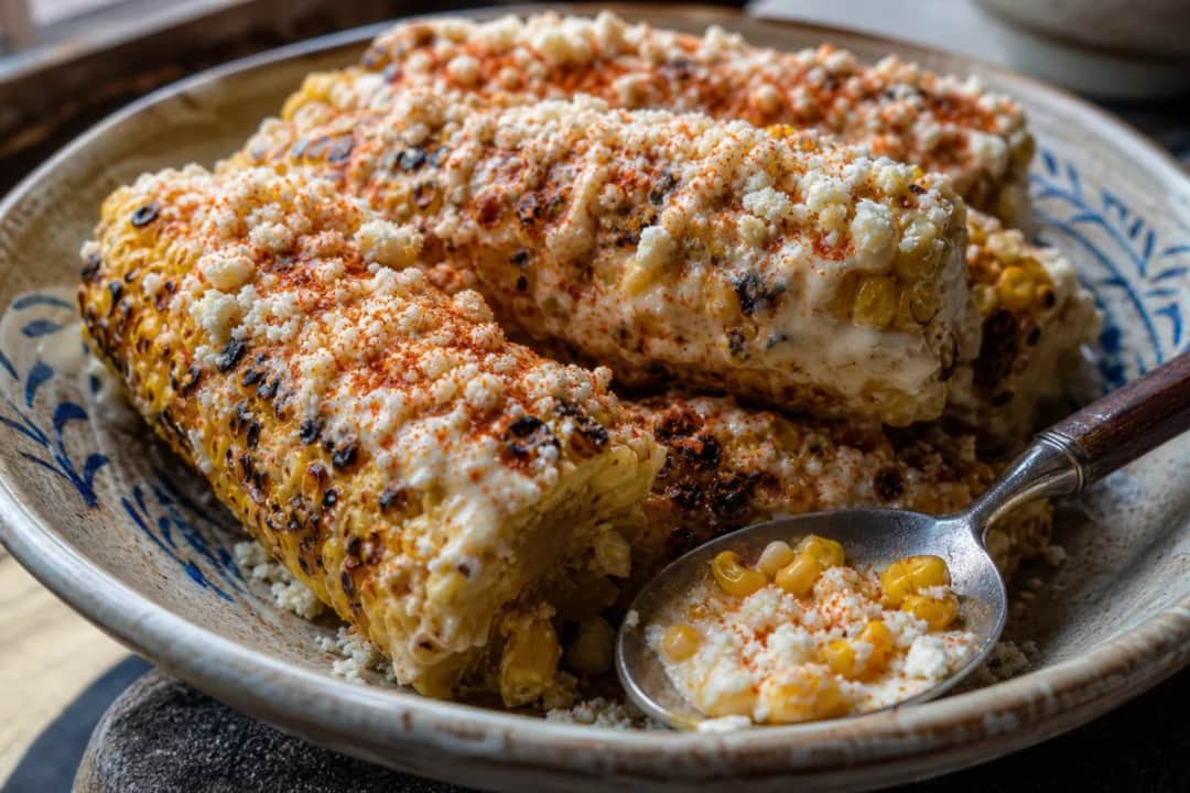 Grilled corn on the cob with creamy cheese topping, sprinkled with chili and cilantro.