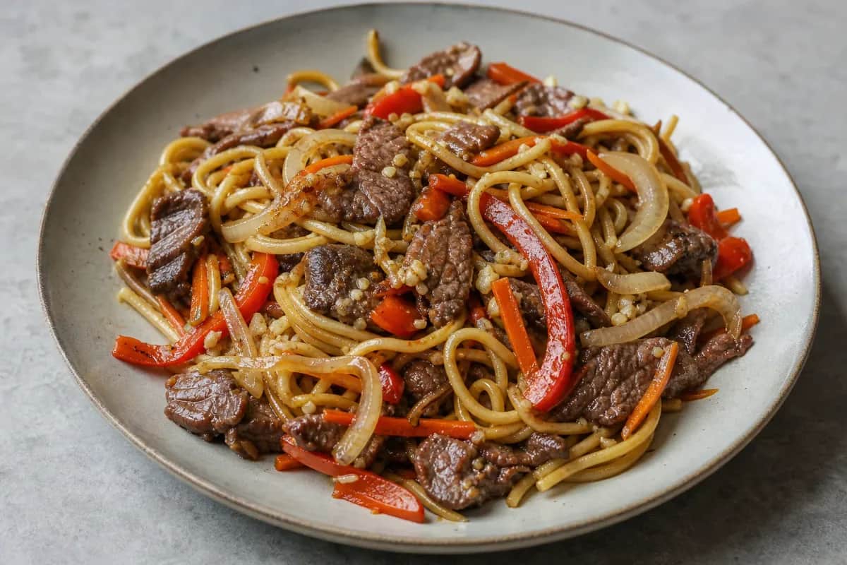 Colorful stir-fried noodles with beef, carrots, and bell peppers in a bowl.