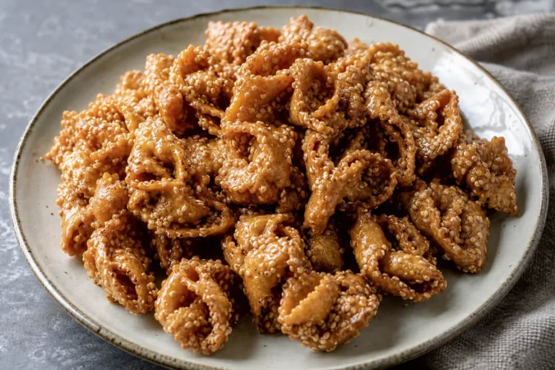 Golden-brown chebakia pastries drizzled with honey, sprinkled with sesame seeds, beautifully arranged on a plate.