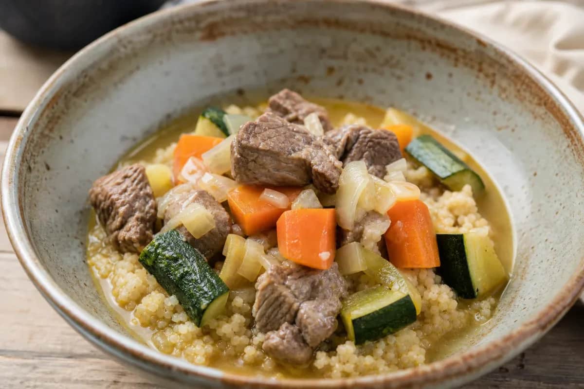 A vibrant plate of Moroccan couscous topped with tender lamb and assorted colorful vegetables.