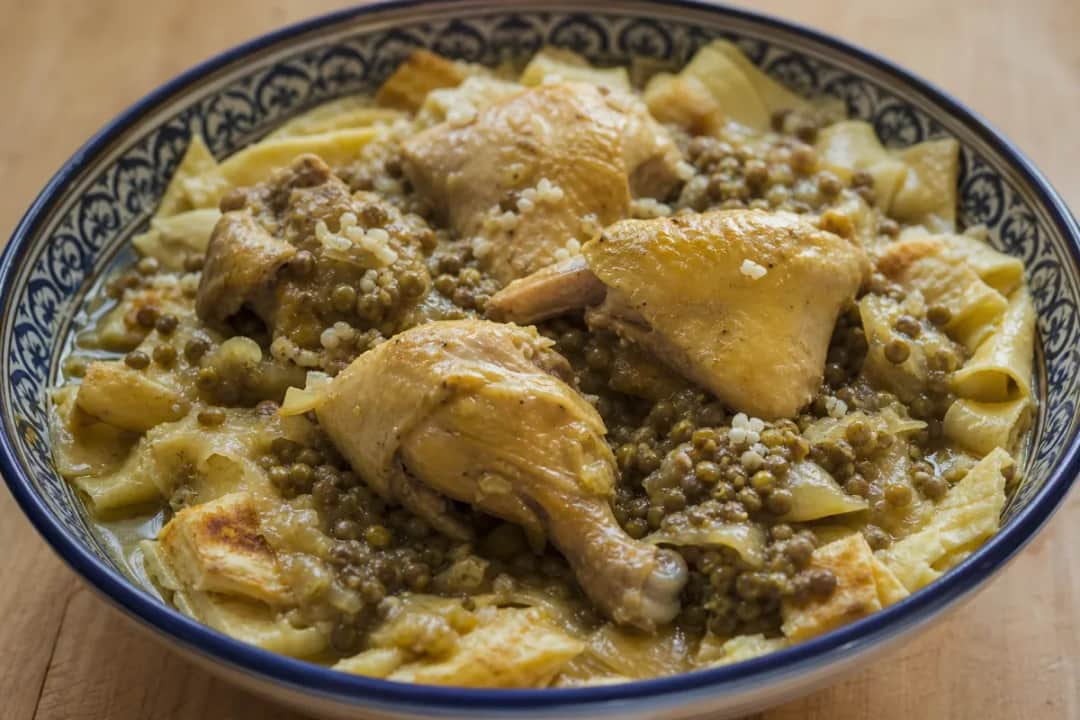 A vibrant plate of Moroccan rfissa showcasing tender chicken, lentils, and layered msemen garnished with fresh herbs.