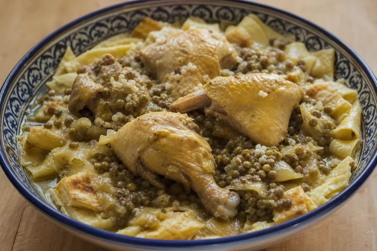 A vibrant plate of Moroccan rfissa showcasing tender chicken, lentils, and layered msemen garnished with fresh herbs.