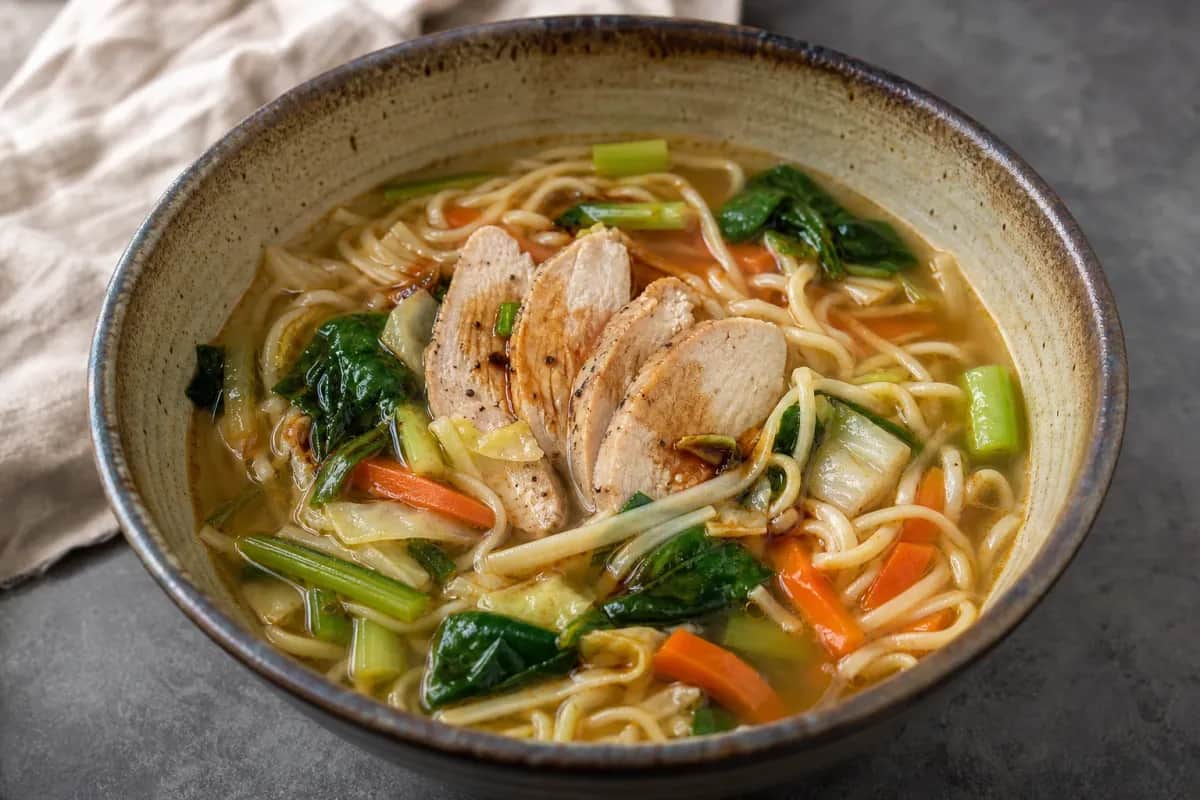 A warm bowl of Thukpa featuring chicken, colorful vegetables, and noodles in a rich broth, garnished with green onions.