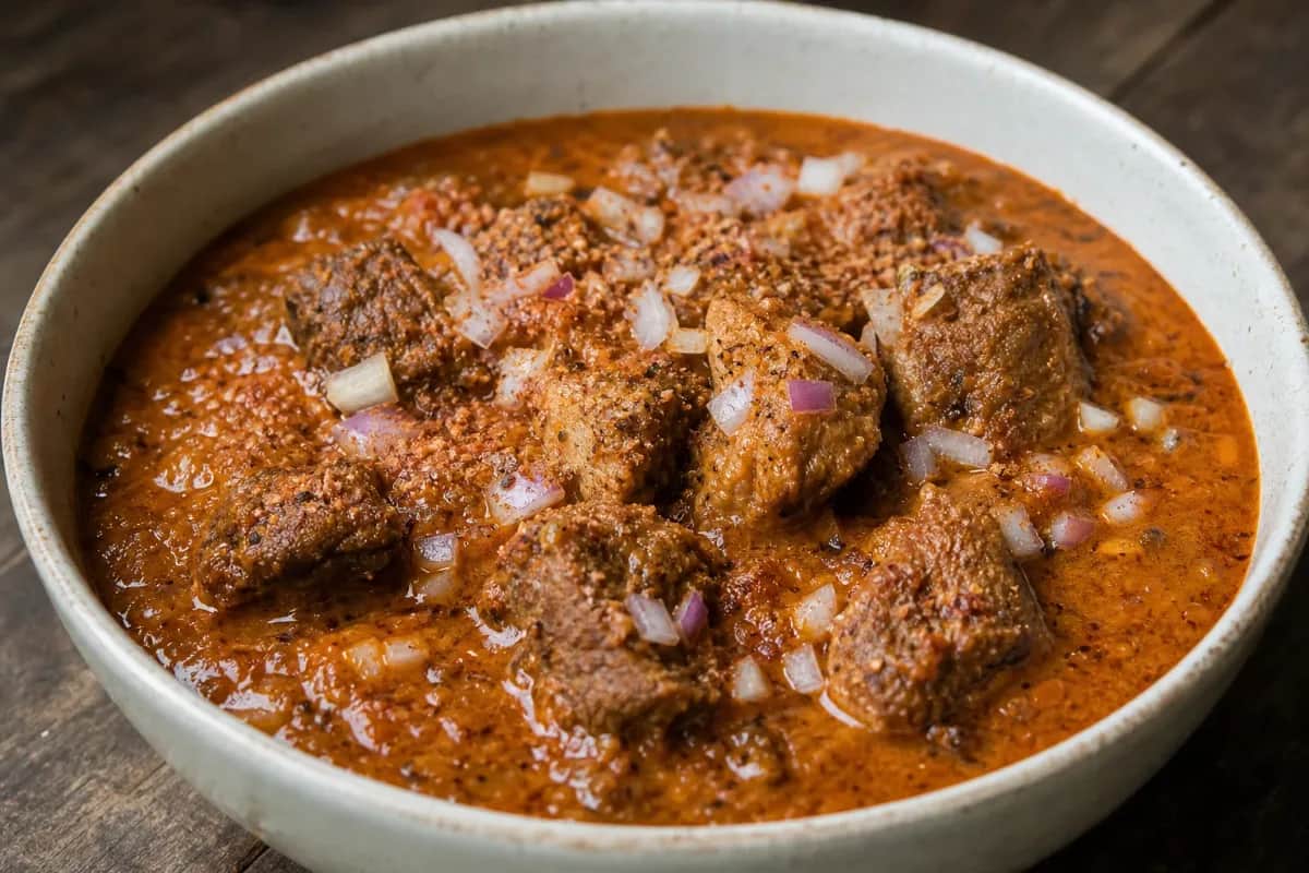 Thick and rich Nigerian Banga Soup garnished with fresh herbs and spices, served in a bowl.