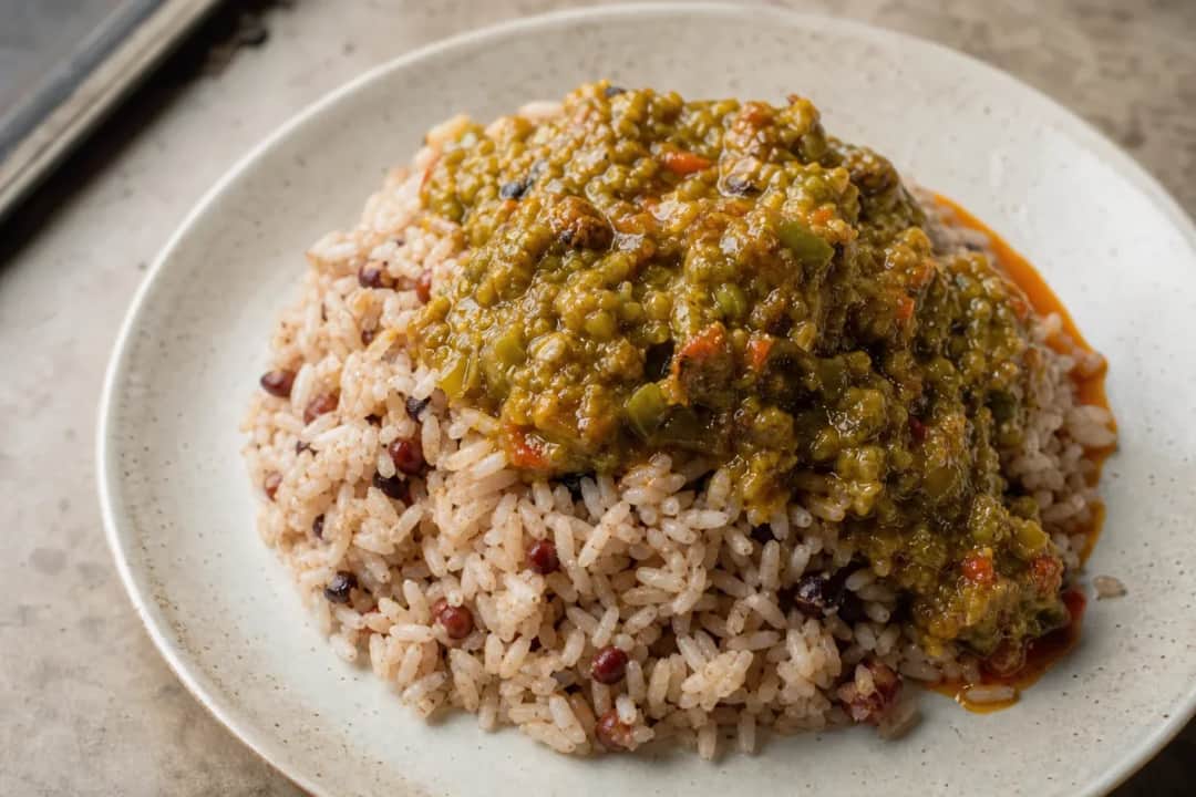 Bowl of Nigerian Ofada rice topped with green Ayamase pepper sauce and garnished with vegetables.