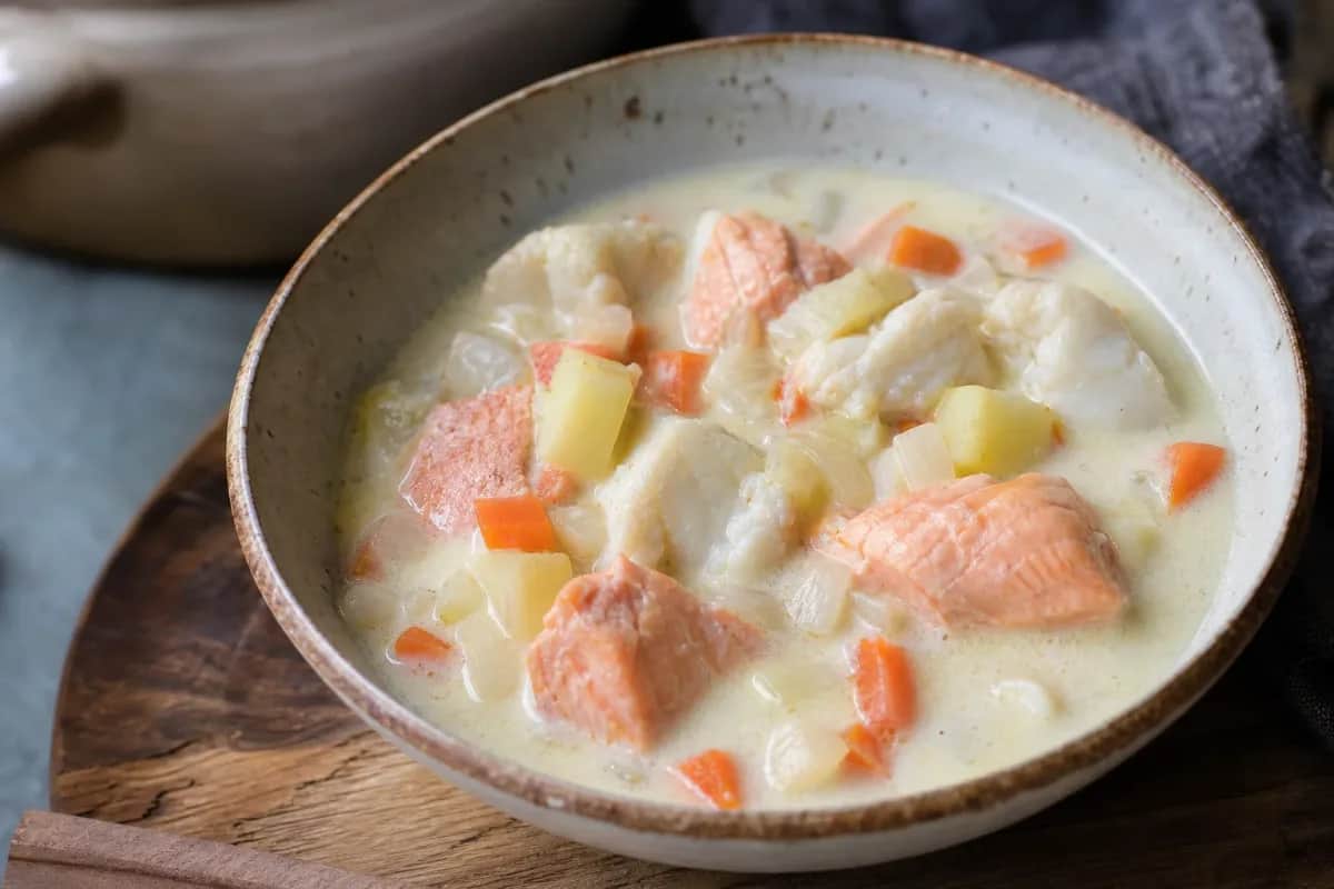 Creamy Norwegian fish soup with salmon, cod, and vegetables, garnished with fresh herbs.