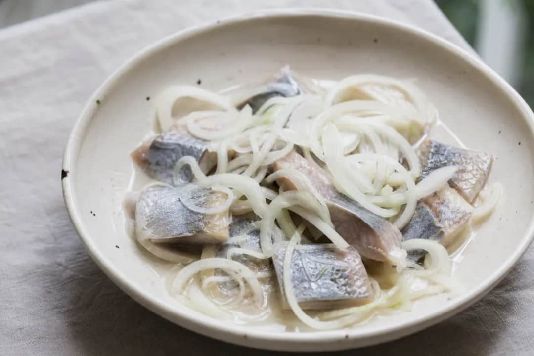 Delicately layered pickled herring garnished with fresh dill and onions, served in a clear dish.