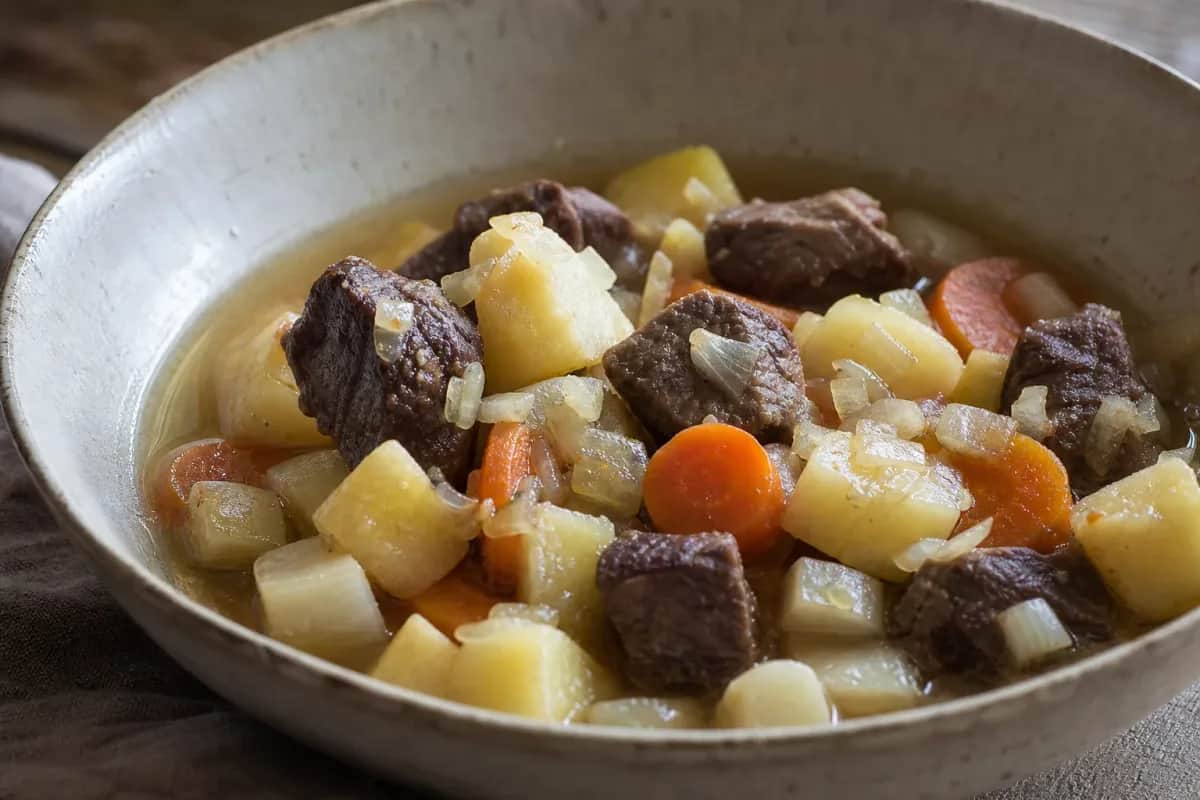 A bowl of thick reindeer stew with carrots, potatoes, and herbs, garnished and steaming.