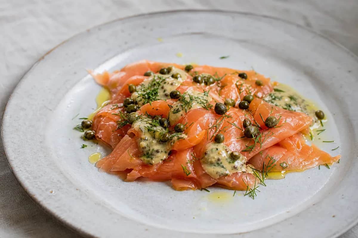 Plated Norwegian smoked salmon garnished with mustard dill sauce and capers, showcasing vibrant colors and textures.
