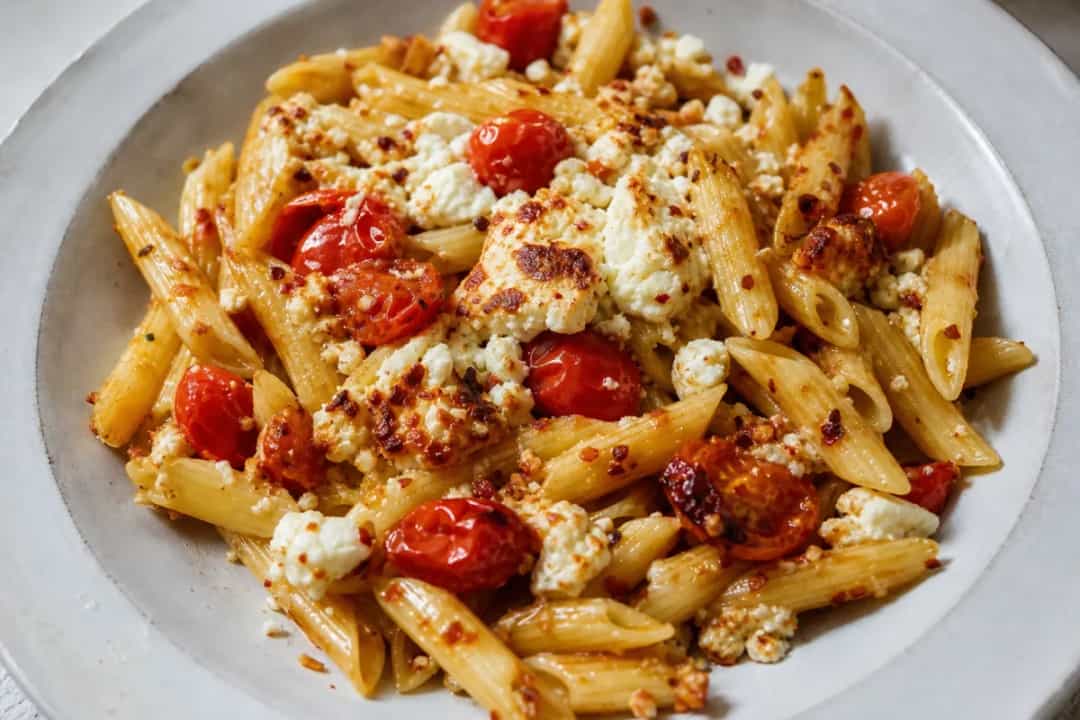 Creamy baked feta pasta with roasted cherry tomatoes and fresh basil on a white plate.