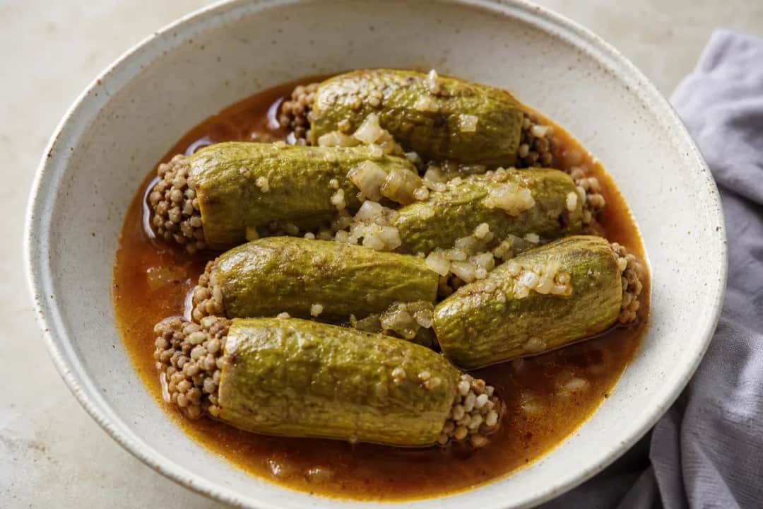Stuffed zucchini in tomato broth, garnished with herbs, showcasing a vibrant color and savory texture.