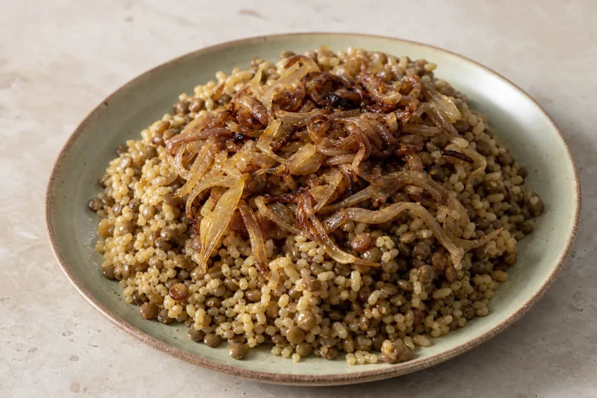 Bowl of Mujaddara featuring lentils, bulgur, and golden caramelized onions garnished with parsley.