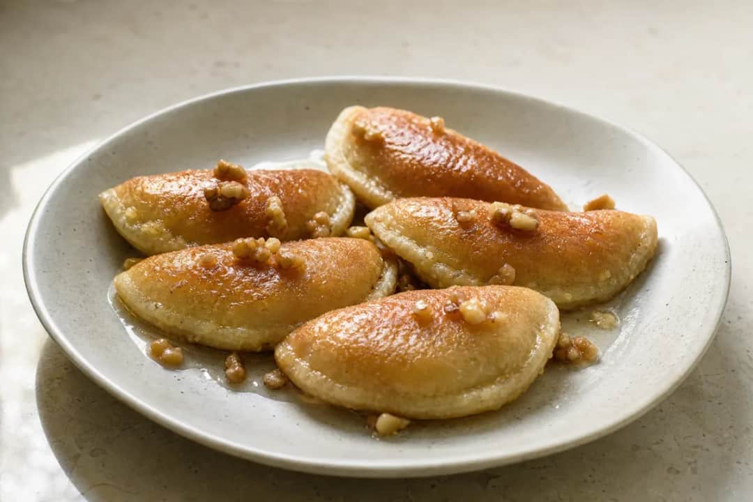 Golden-brown qatayef stuffed with walnuts, drizzled in syrup, plated beautifully.