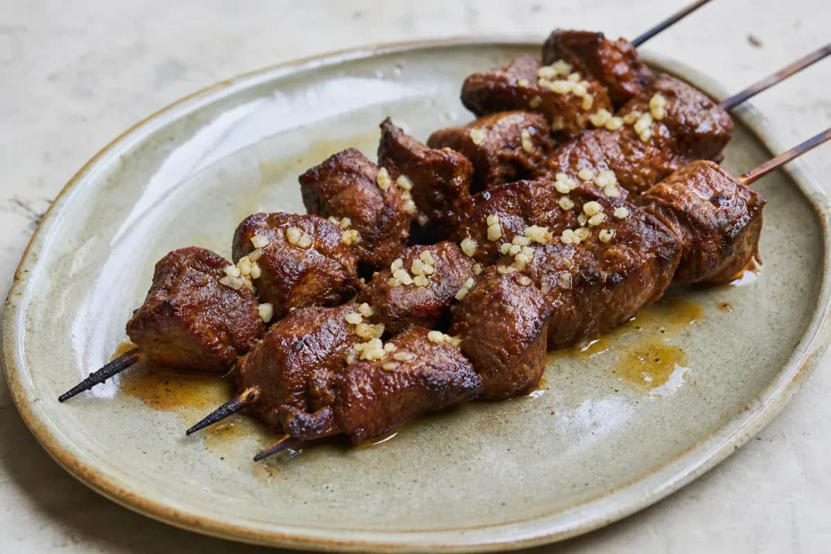 Skewered marinated beef with aji panca sauce garnished with herbs and served on a plate.