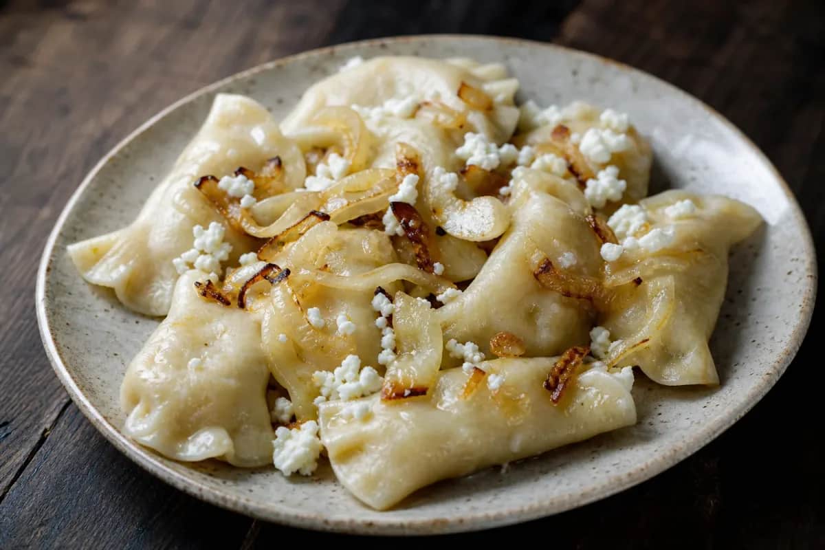 Golden brown pierogi filled with potato and cheese, garnished with caramelized onions on a white plate.
