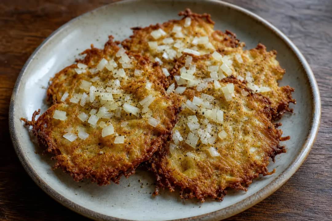 Golden brown potato pancakes topped with sour cream and chives on a white plate.