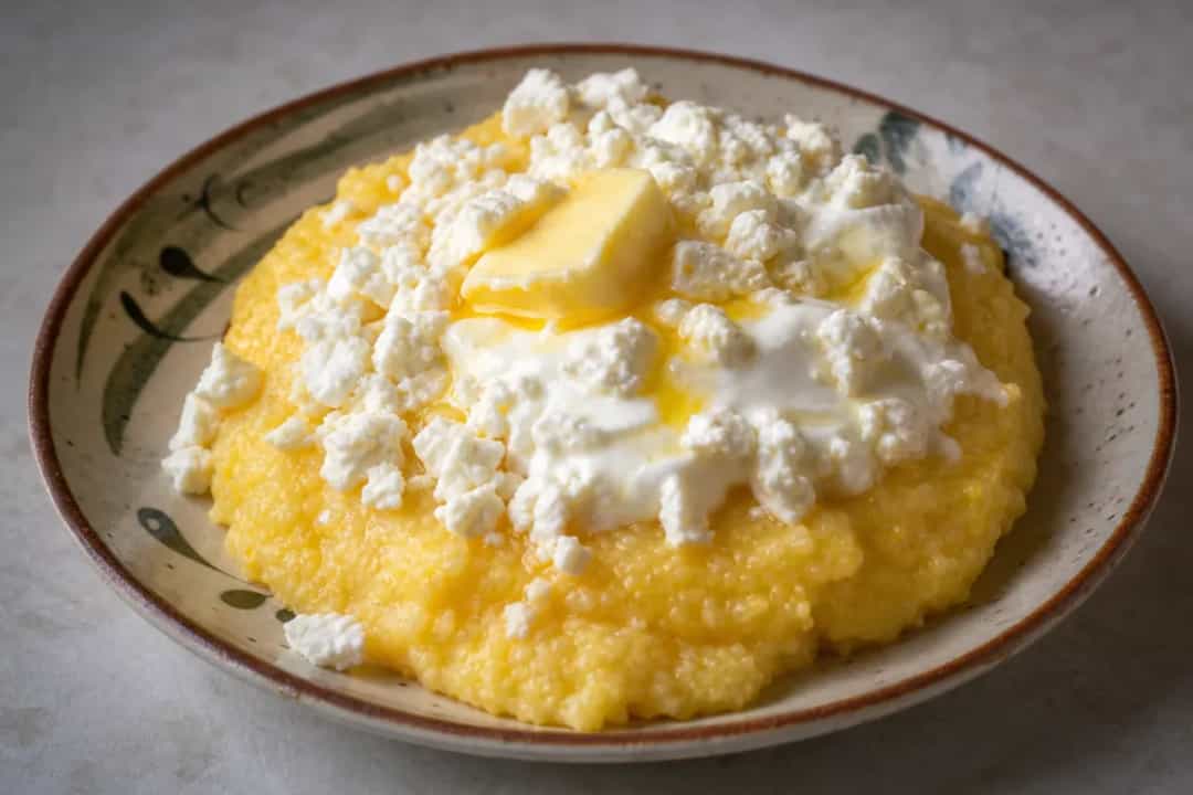 Creamy cornmeal mămăligă topped with melted cheese and sour cream, served warm.