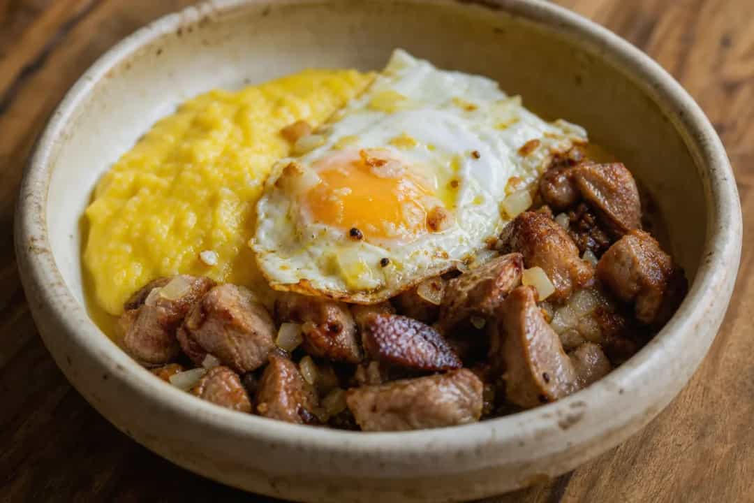 A plate of Romanian Tochitură featuring tender pork, creamy polenta, and a perfectly fried egg on top.