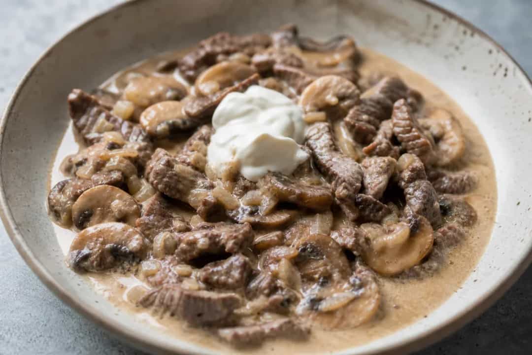 Plate of beef stroganoff garnished with parsley, showcasing creamy sauce and tender mushrooms.