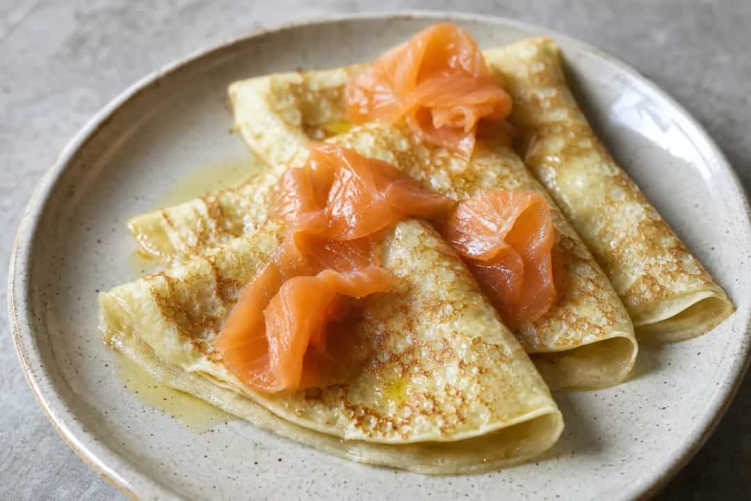 Delicately stacked blini topped with smoked salmon and creamy sour cream, garnished with fresh herbs.