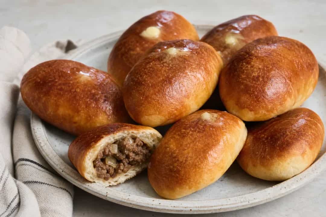 Golden-brown pirozhki stuffed with beef and onion, arranged on a plate.