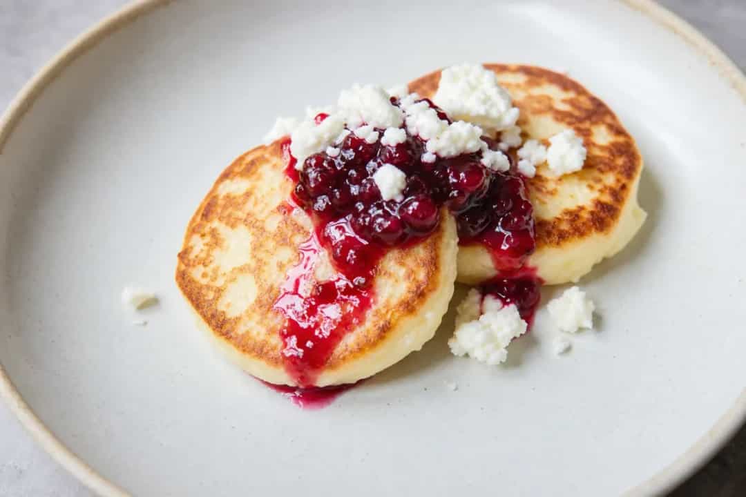 Golden-brown syrniki pancakes topped with berry sauce and fresh mint.