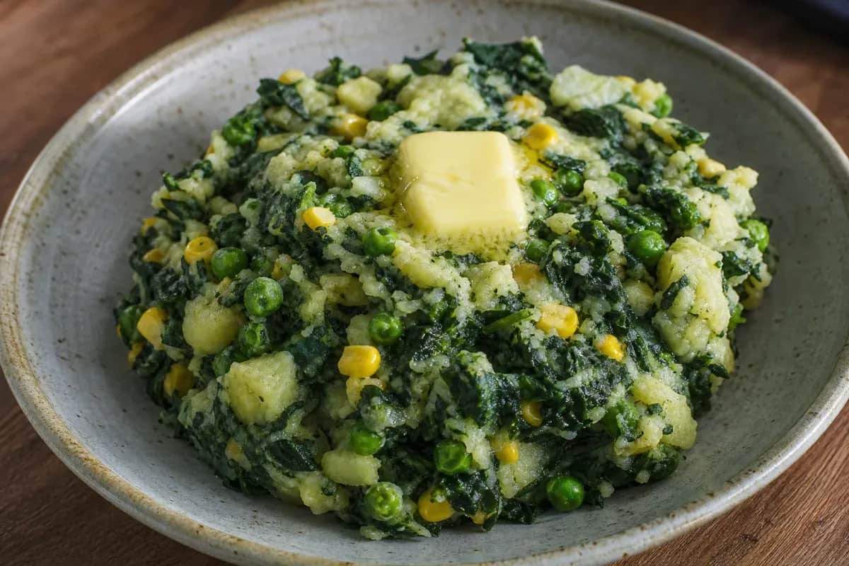 A vibrant plate of Mukimo showcasing creamy potatoes, green vegetables, and colorful peas, garnished for an inviting look.