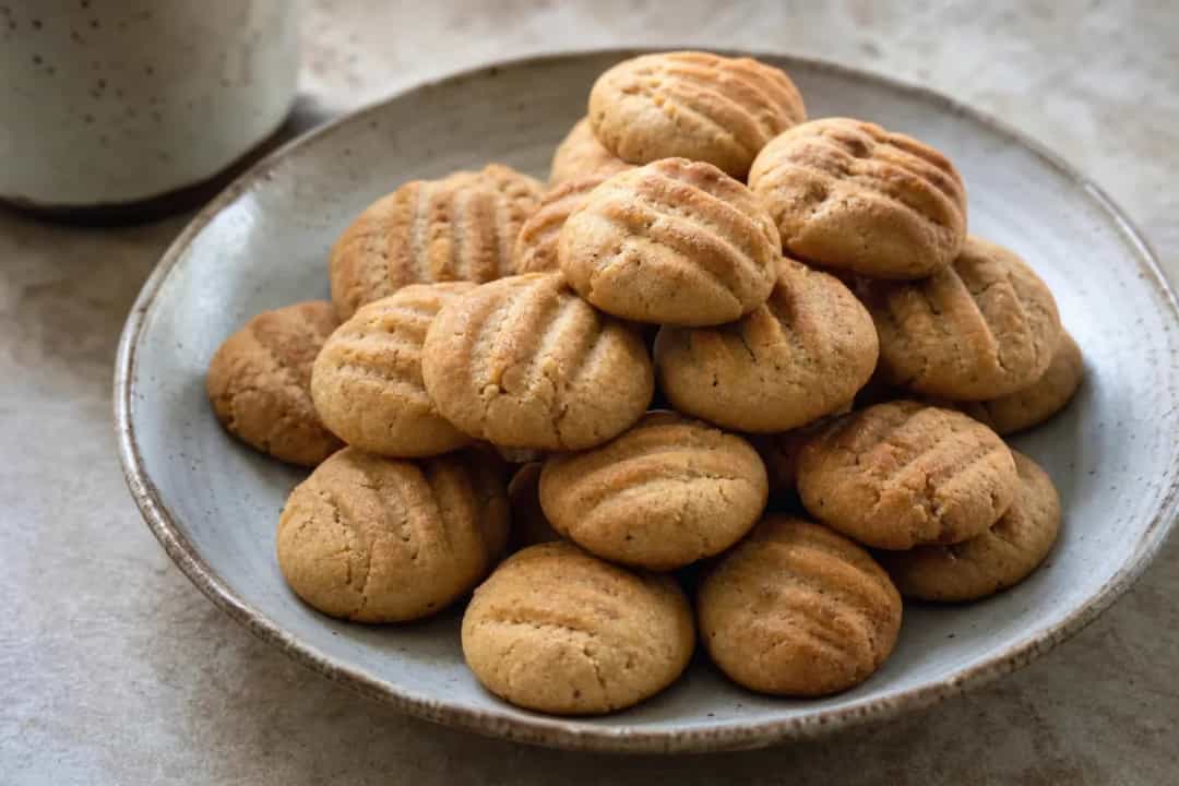 Golden-brown kleija cookies dusted with powdered sugar, featuring cardamom seeds and cinnamon.