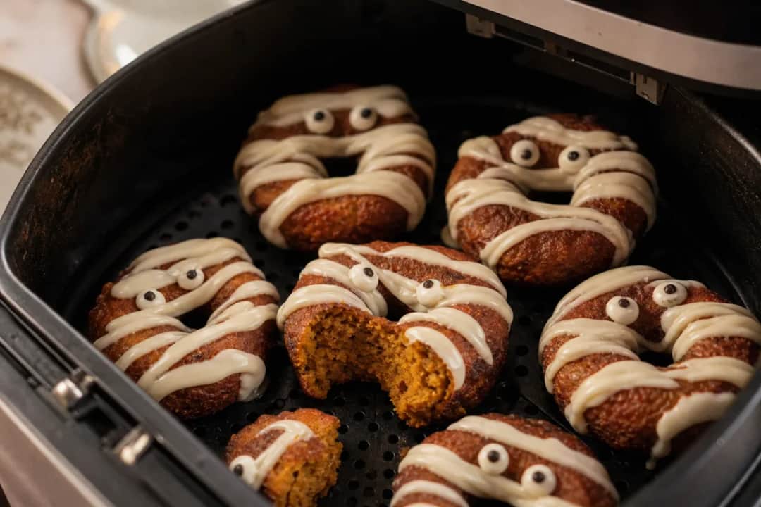 Plated pumpkin spice doughnuts with mummy icing and decorative eyes, showing a soft texture.