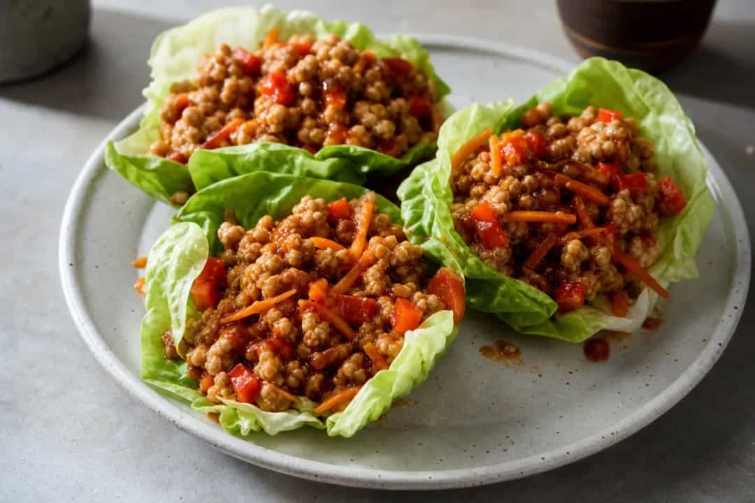 Crisp lettuce wraps filled with spicy Sriracha honey chicken, colorful vegetables, and garnished with sesame seeds.