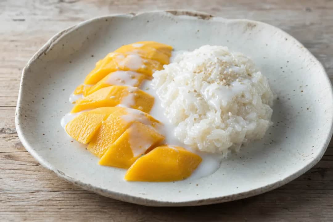 Plated Thai mango sticky rice with coconut sauce and fresh mango slices, showcasing a glossy texture and vibrant colors.
